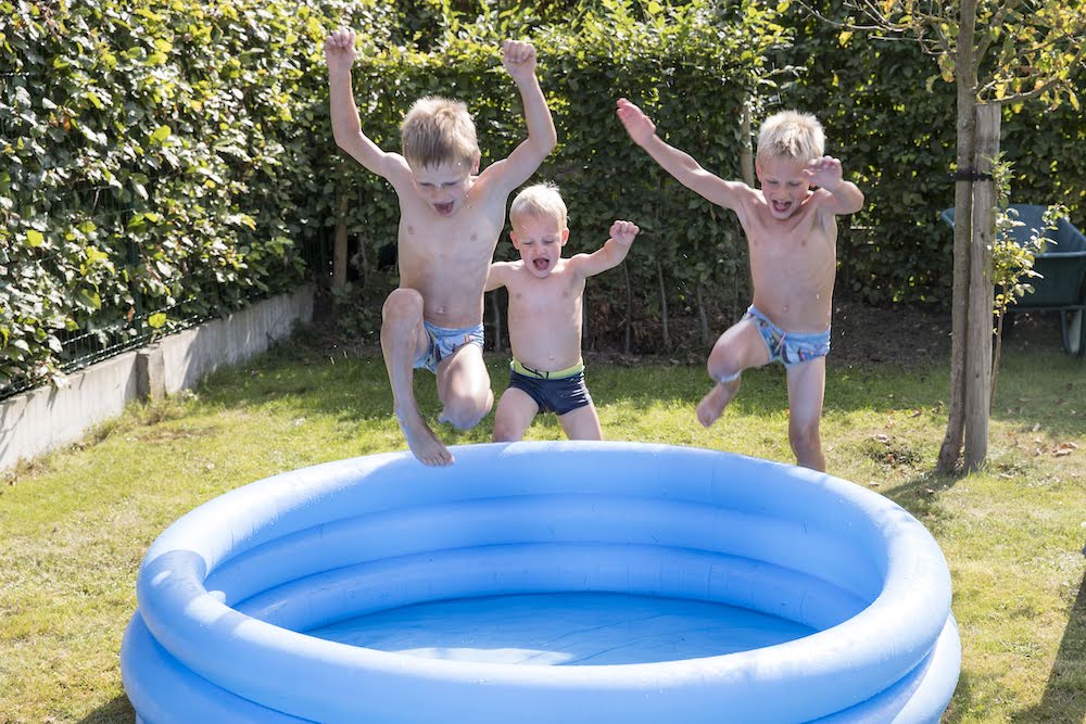 jongens springen in een opblaasbaar zwembadje in de tuin