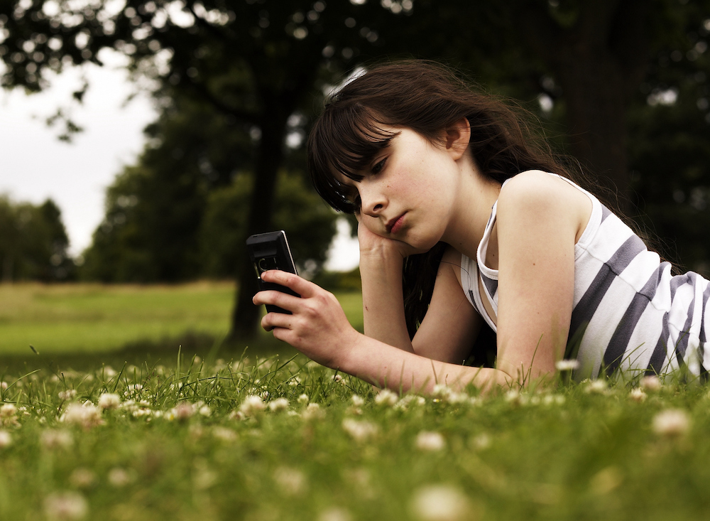 tienermeisje ligt in he gras met smartphone