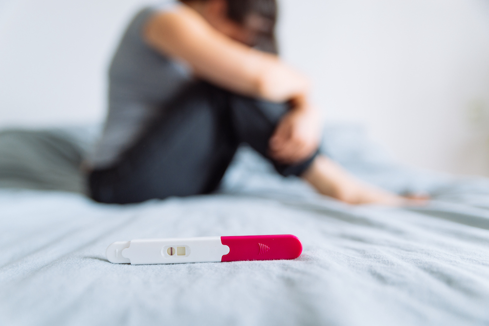 vrouw zit op bed met negatieve zwangerschapstest