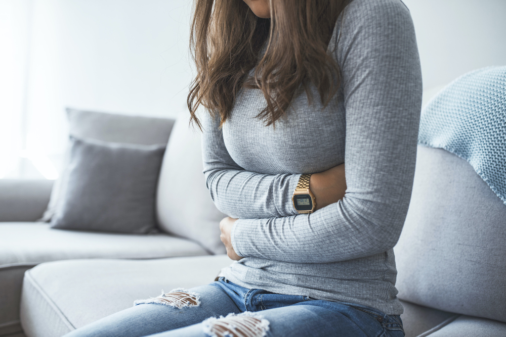 vrouw zit op de zetel en heeft buikpijn