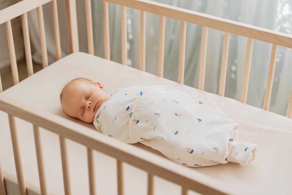 Baby slaapt in inbakerslaapzak in bedje