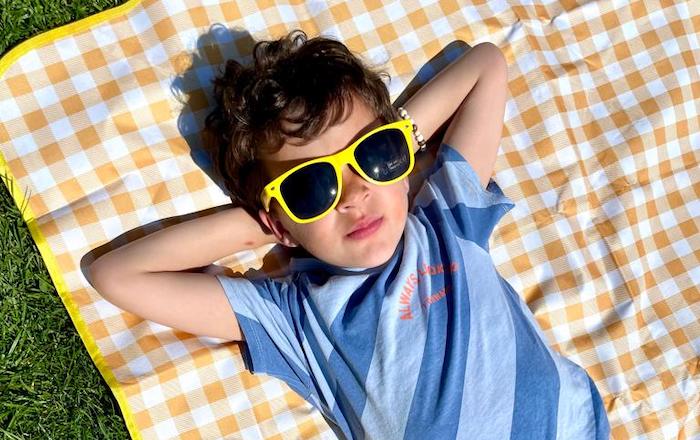 Jongen ligt op picknickdeken en met zonnebril in de zon