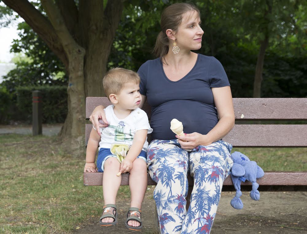 Zwangere mama zit met zoontje op bank en houdt ijsje vast