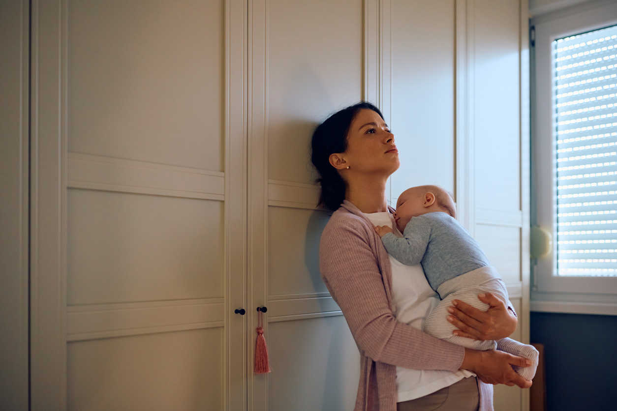 Mama met baby in haar armen leunt tegen kast