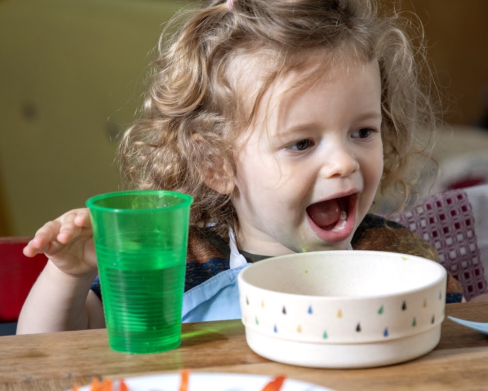 peuter zit aan tafel met bordje en beker voor zich