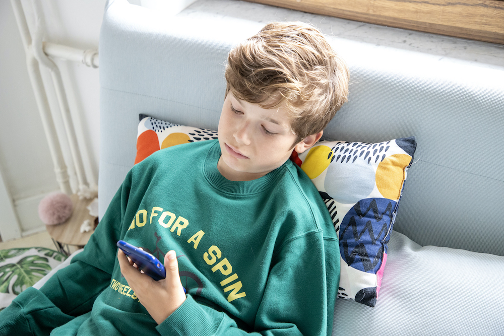 Tienerjongen ligt in de zetel en kijkt op smartphone