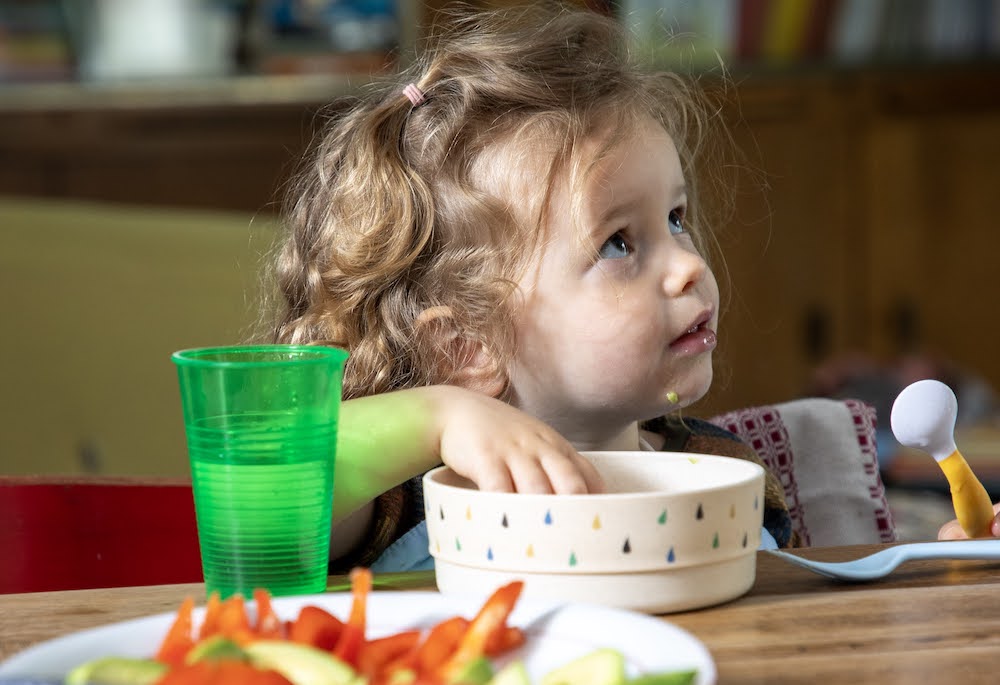peuter zit aan tafel met bordje en beker met water