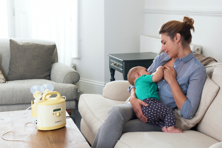 Mama geeft baby borstvoeding, borstkolf staat op tafel