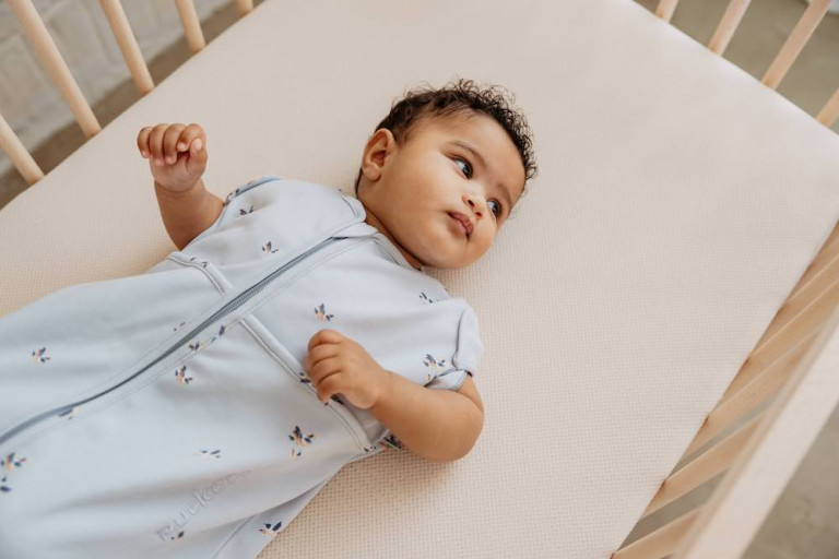 Baby ligt in slaapzak in bedje