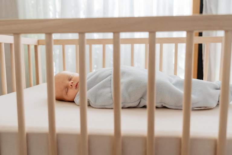 Baby slaapt in inbakerslaapzak in bedje