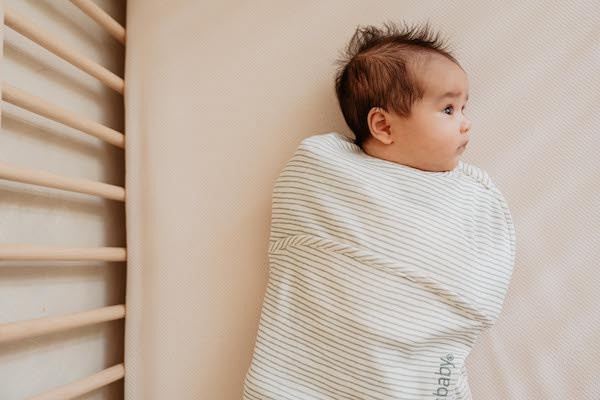 Baby ligt in bek in inbakerslaapzak