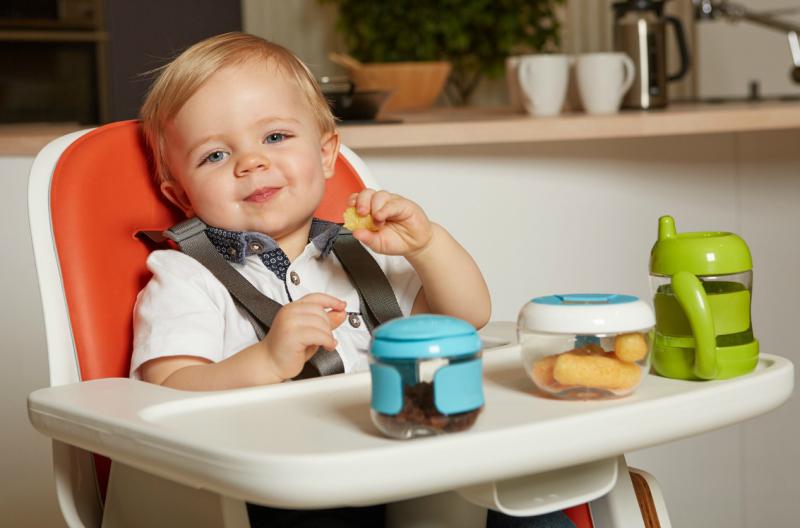 Kindje aan het eten met bordje, doosje en beker in de stoel