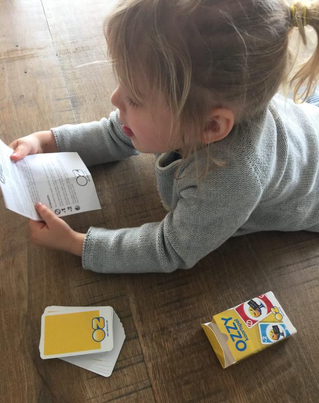 meisje met papier in de hand en kaartspel OZ Ozzy naast haar