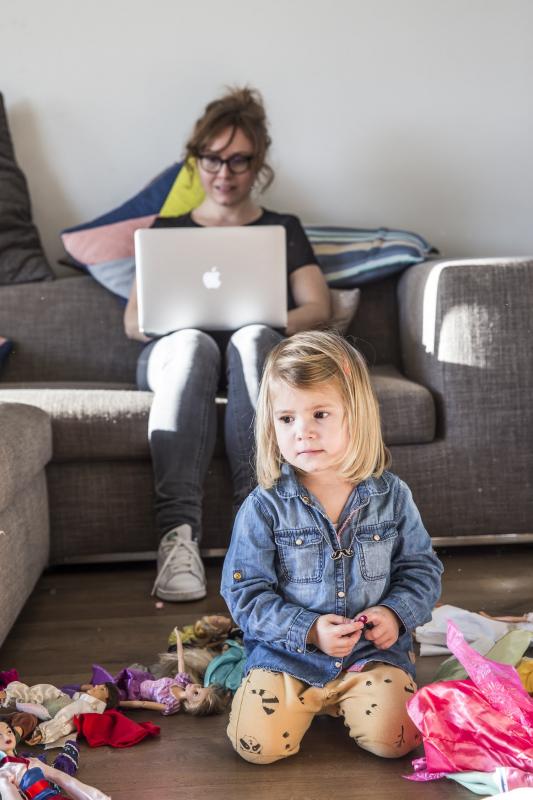 Mama werkt in de zetel, kindje speelt