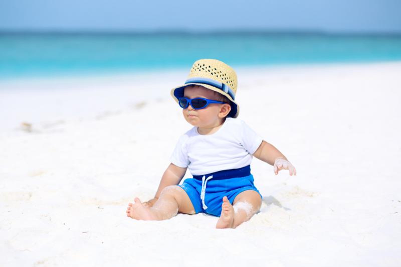 baby jongen op strand met zonnebril en hoed
